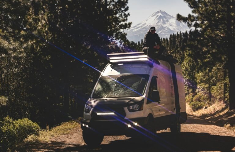 A man sitting on top of a van on a dirt road